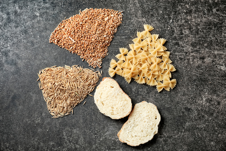 Raw wheat, oats, pasta and slices of bread on grey tableの写真素材