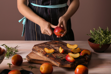 Woman cutting fresh sweet peaches at wooden tableの写真素材