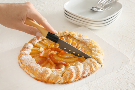 Woman cutting delicious peach galette on board, closeupの写真素材