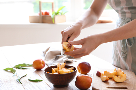 Woman cutting fresh sweet peaches at wooden tableの写真素材