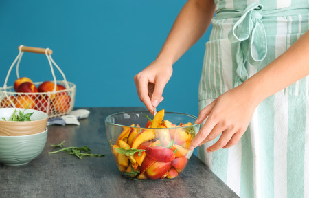 Woman preparing tasty salad with sliced peaches and arugulaの写真素材