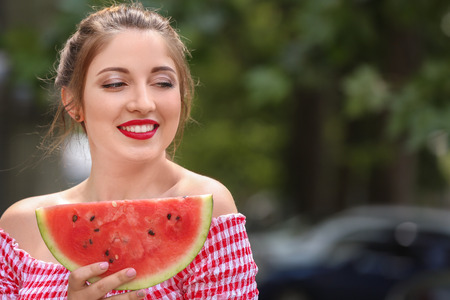 Beautiful young woman with slice of tasty watermelon outdoorsの写真素材