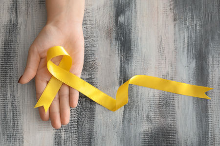 Woman holding yellow ribbon on wooden background. Cancer awareness conceptの写真素材
