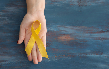 Woman holding yellow ribbon on wooden background. Cancer awareness conceptの写真素材
