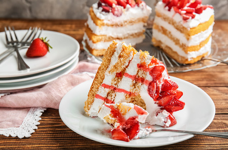 Plate with piece of delicious strawberry cake on wooden table