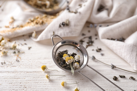 Sieve with dried chamomile and tea leaves on white wooden tableの写真素材
