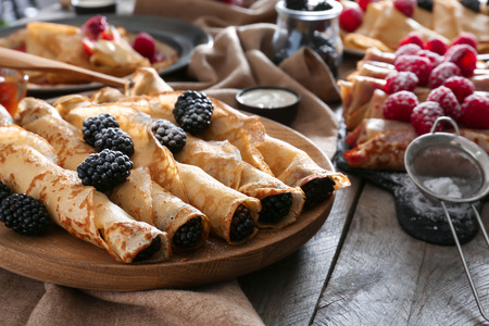 Plate with tasty thin pancakes and berries on wooden tableの写真素材