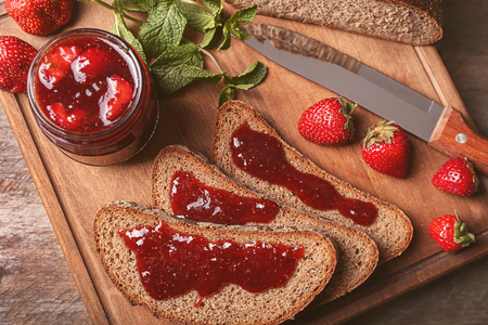Board with slices of bread and delicious strawberry jam on wooden tableの写真素材