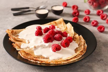 Plate with tasty thin pancakes and berries on light tableの写真素材