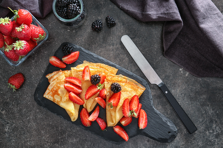 Slate board with tasty thin pancakes and berries on dark tableの写真素材