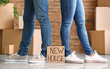 Legs of young couple and cardboard sheet with text NEW HOUSE indoorsの写真素材
