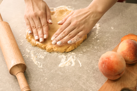 Woman preparing dough for peach galette at tableの写真素材