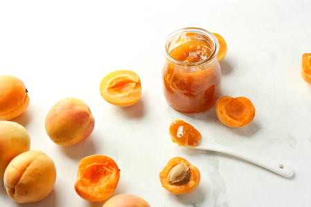 Jar with delicious apricot jam and fresh fruit on light tableの写真素材