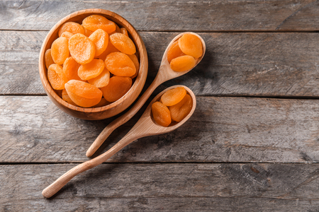 Bowl and spoons with dried apricots on wooden tableの写真素材