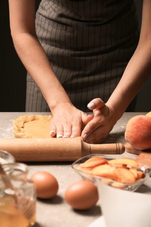 Woman preparing dough for peach galette at tableの写真素材