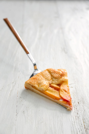 Shovel with piece of delicious peach galette on white wooden tableの写真素材