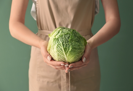 Woman holding fresh cabbage on color background