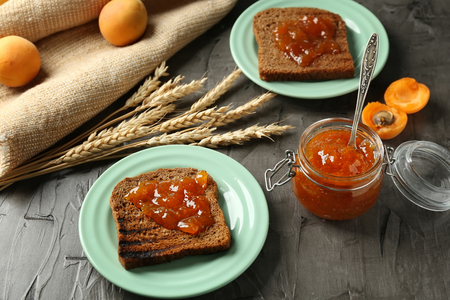 Jar with delicious apricot jam and sliced bread on tableの写真素材