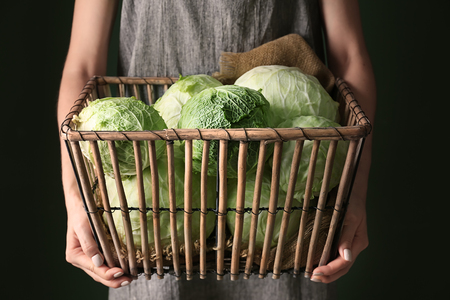 Woman holding basket with fresh cabbage on dark backgroundの写真素材