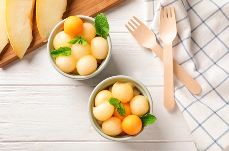 Delicious melon balls in bowls on white wooden tableの写真素材