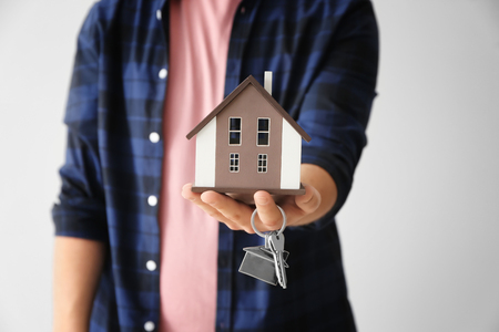 Man holding house model and key on light background, closeup. Mortgage conceptの写真素材