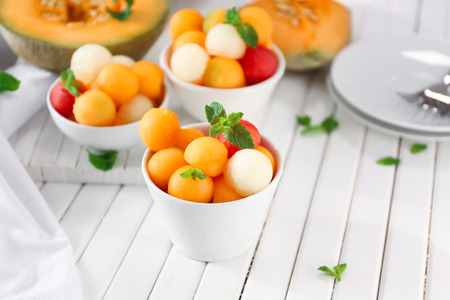 Bowls with tasty melon dessert on white wooden tableの写真素材