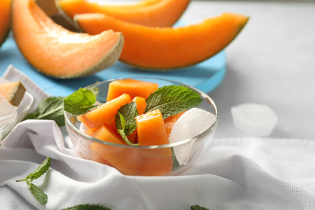 Glass bowl with pieces of melon and ice cubes on tableの写真素材