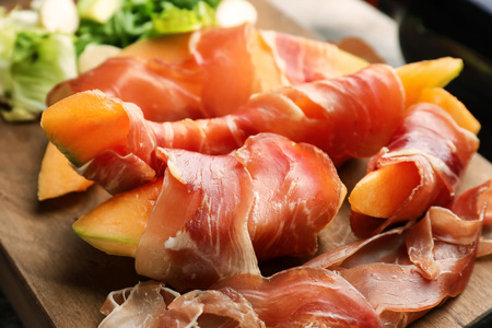Delicious melon wrapped in prosciutto on wooden board, closeupの写真素材