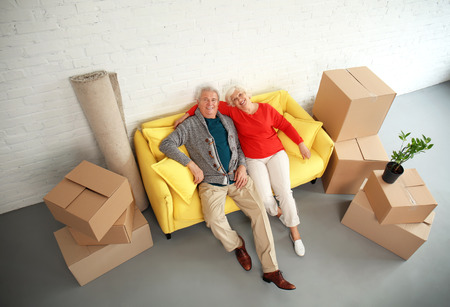 Mature couple sitting on sofa near boxes after moving into new house