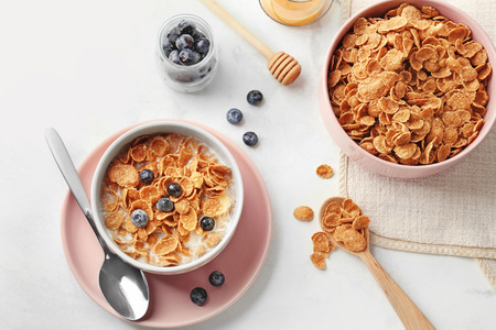 Bowls with healthy cornflakes, milk and blueberry on white table
