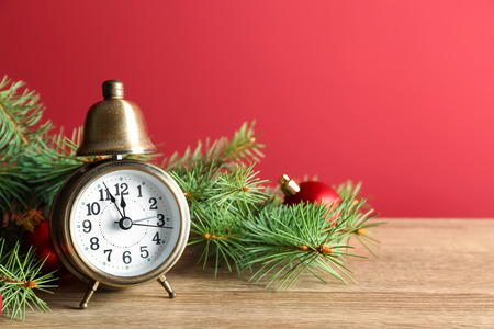 Alarm clock with fir branches on wooden table against color background. Christmas countdownの写真素材