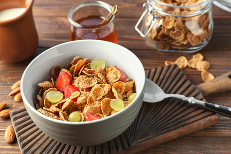 Tasty corn flakes with strawberry and grape in bowl on wooden table