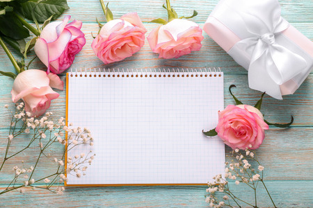 Beautiful roses, gift box and notebook on wooden tableの写真素材
