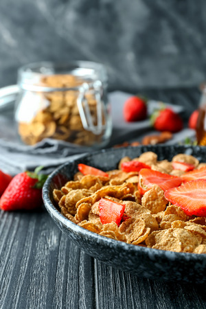 Plate with tasty corn flakes and strawberry on dark tableの写真素材