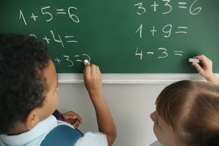 Schoolchildren writing on chalkboard in classroom during math lessonの写真素材