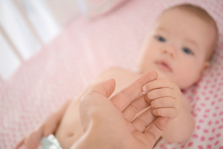 Cute baby holding mother's hand while lying on bedの写真素材