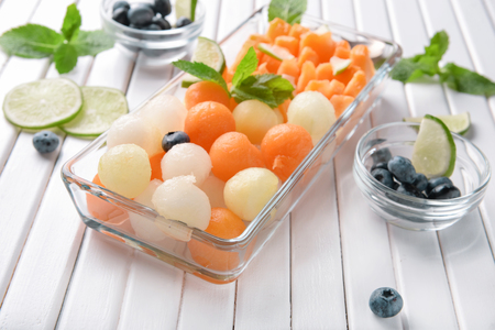 Plate with delicious melon balls and berries on white wooden tableの写真素材