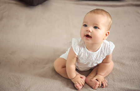 Adorable baby sitting on bed at home