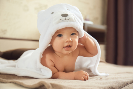 Cute baby with towel lying on bed at homeの写真素材