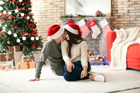 Portrait of cute young couple in Santa hats at home on Christmas eveの写真素材