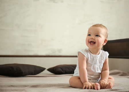 Adorable baby sitting on bed at homeの写真素材