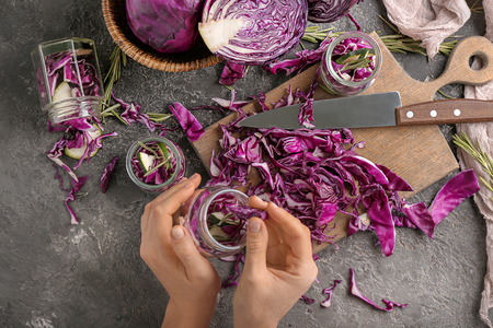 Woman putting cut red cabbage into glass jar on grunge tableの写真素材