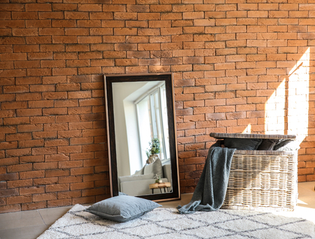 Big stylish mirror with wicker basket near brick wall in roomの写真素材