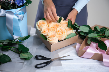 Female florist preparing box with beautiful flowers at tableの写真素材