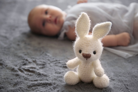 Bunny toy near cute little baby lying on bedの写真素材