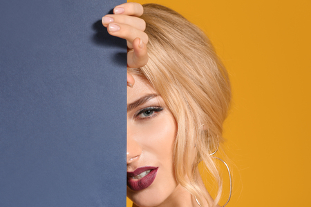 Beautiful young woman with dark lipstick and poster on color backgroundの写真素材