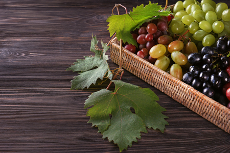 Wicker basket with fresh ripe grapes on wooden tableの写真素材