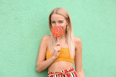 Beautiful young woman with lollipop near color wallの写真素材