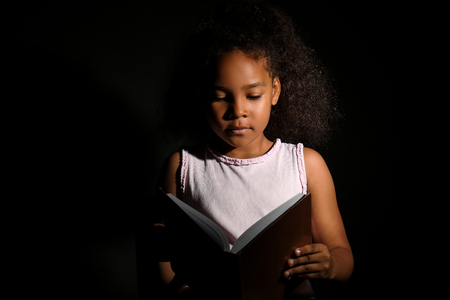 Little African-American girl reading book on dark backgroundの写真素材