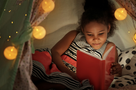 Little African-American girl reading bedtime story in hovelの写真素材